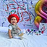 toddler, child, red_beret, black_and_white_dress, white_blanket, paint_brushes, paint_pots, canvas, abstract_art, colorful_paint, balloon, number_8, smiling, happy, sitting, indoors, creative, artistic, festive, portrait