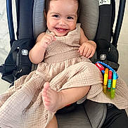 Gemma is registered to the contest to win money with this photo: baby, smile, car_seat, dress, toy, child, happy, infant, cute, foot, hand, indoors, seatbelt, play, colorful, person, portrait, infant_clothing, baby_toy, car_seat_accessory