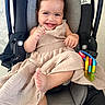 baby, smile, car_seat, dress, toy, child, happy, infant, cute, foot, hand, indoors, seatbelt, play, colorful, person, portrait, infant_clothing, baby_toy, car_seat_accessory