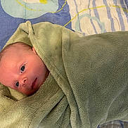 Hugo a rejoint le concours — aidez-le/la à gagner de superbes lots ! newborn, baby, blanket, green_blanket, wrapped, lying_down, infant, face, eyes, soft_texture, cozy, cute, indoor, patterned_background, blue_background, yellow_detail, skin, head, person, child