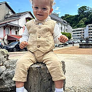 Leeroy participe au concours pour gagner de l'argent avec cette photo : beige_clothing, bow_tie, buildings, cars, child, curly_hair, daytime, happy, outdoor, pants, portrait, rock, sky, smiling, toddler, trees, urban, vest, white_shoes, white_socks