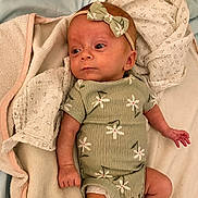 Allie is registered to the contest to win money with this photo: baby, infant, child, green_onesie, headband, bow, blanket, soft_texture, cute, newborn, lying_down, clothing, patterned, floral, sleepwear, indoors, skin, hand, face, portrait