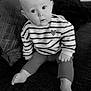 baby, child, striped_sweater, heart_patch, couch, indoor, black_and_white, curious, wide_eyes, seated, foot, hand, cozy, portrait, infant, expression, soft_lighting, home, cute, casual_clothing