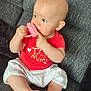 baby, child, infant, red_shirt, white_pants, toy, pink_toy, couch, gray_couch, sitting, barefoot, curious, indoors, soft_lighting, cute, chubby_cheeks, portrait, young_child, home, relaxed
