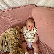Romey is registered to the contest to win money with this photo: baby, infant, stuffed_animal, plush_toy, pink_blanket, sitting, cute, child, soft_texture, indoors, cozy, white_clothing, socks, toy, young_child, portrait, relaxed, comfort, small_person, furniture