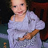 toddler, child, curly_hair, smiling, gray_hoodie, oversized_clothing, red_chair, indoor, portrait, cute, young_child, happy, casual_wear, standing, person, clothing, face, eyes, nostalgic, timestamp