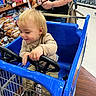 adult, aisle, bag_of_potatoes, blonde_hair, child, clothing, floor, grocery_store, hand, happy, person, shoes, shopping, shopping_cart, smile, steering_wheel, supermarket, tattoo, toddler, toy_car