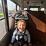 child, bus, seat, harness, smiling, sunlight, window, seatbelt, young, boy, casual_clothing, indoor, transportation, safety, happy, daylight, portrait, seat_back, vehicle, hair
