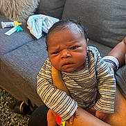 James is registered to the contest to win money with this photo: baby, infant, striped_clothing, person, couch, living_room, arm, hospital_wristband, hand, face, expression, furniture, pillow, blanket, indoor, skin, newborn, holding, carpet, footwear