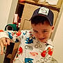 child, boy, hoodie, cap, sonic_the_hedgehog, cartoon_clothing, indoor, playful, smiling, young, clutter, boxes, cardboard, casual, portrait, person, messy_background, expression, fun, hat