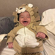 Dakota is registered to the contest to win money with this photo: baby, lion_costume, smiling, happy, cute, infant, hooded_outfit, bed, pillow, blanket, indoor, child, person, cozy, plush, cute_animal_costume, soft_fabric, young_child, portrait, playful