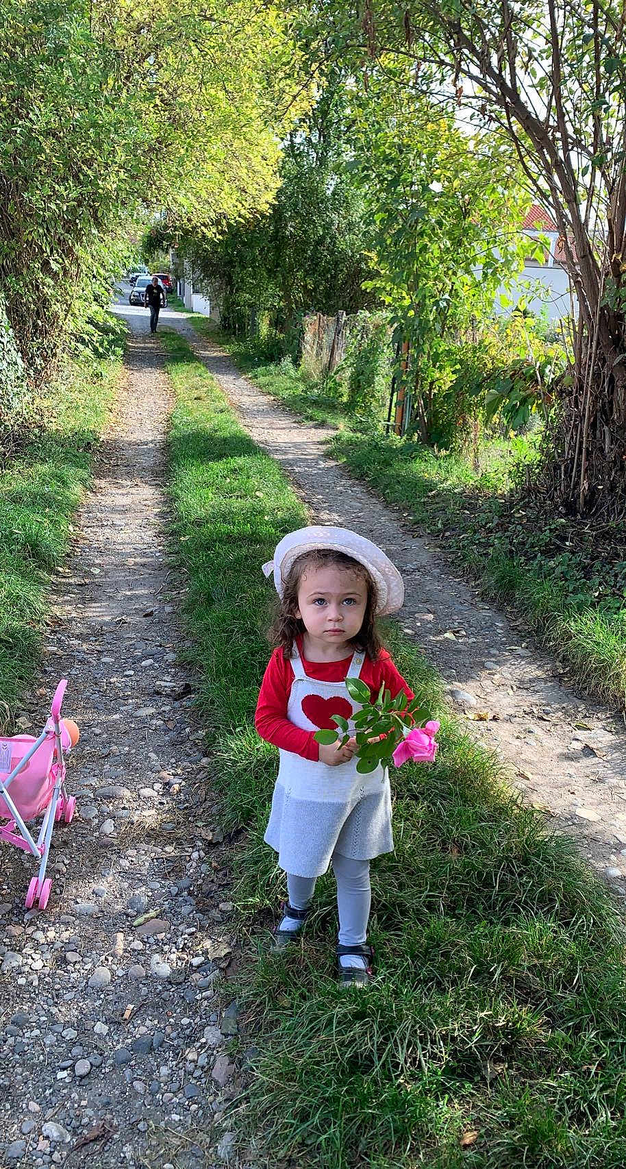 Mélina a rejoint le concours — aidez-le/la à gagner de superbes lots ! child, girl, flower, hat, dress, grass, path, stroller, toy, nature, outdoor, tree, greenery, person, walking, sunlight, leafy, casual, curly_hair, shoes