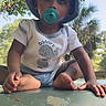 toddler, child, baby, sitting, outdoor, portrait, bucket_hat, pacifier, smiling, face, hands, barefoot, clothing, shirt, shorts, table, trees, palm_trees, sunlight, warning_sign