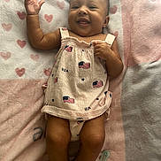 Aaliyah is registered to the contest to win money with this photo: baby, infant, smiling, lying_down, blanket, hearts_pattern, dress, usa_flag, pacifier, happy, cute, child, skin, hand, foot, indoors, fabric, soft, portrait, person
