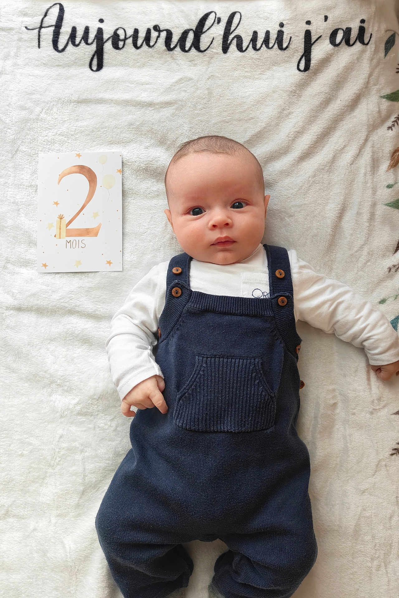 Ulysse a rejoint le concours — aidez-le/la à gagner de superbes lots ! baby, infant, child, milestone_card, two_months, blanket, onesie, overalls, buttons, portrait, lying_down, wide_eyes, hand, soft_texture, card, text_on_blanket, indoor, neutral_background, cute, photography