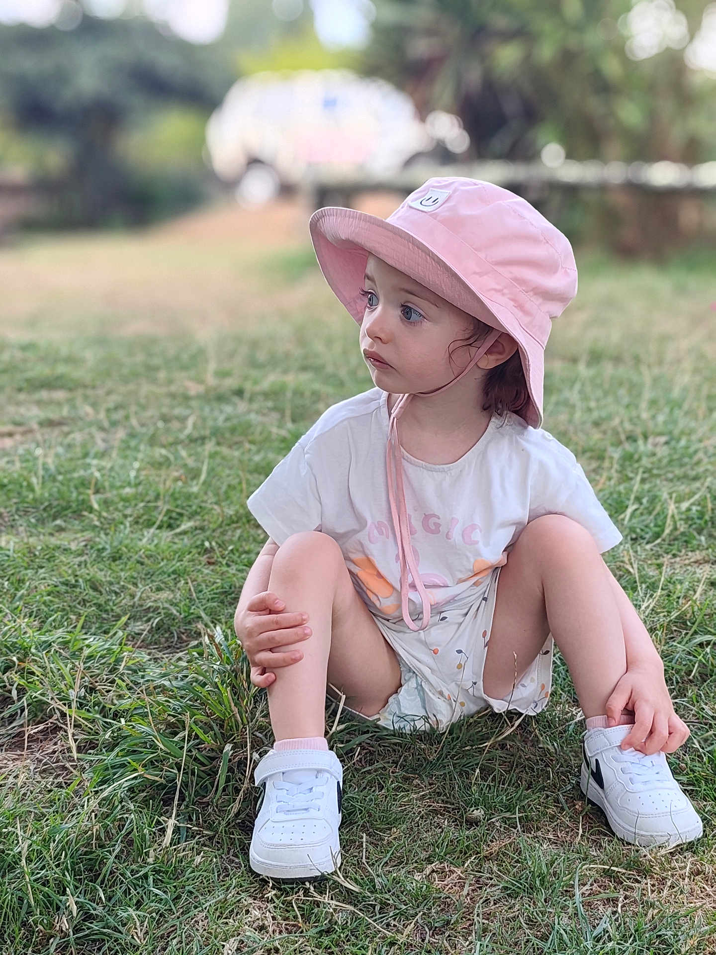 Victoire participe au concours pour gagner de l'argent avec cette photo : child, toddler, grass, outdoor, hat, bucket_hat, white_sneakers, sitting, curious, casual_clothing, nature, daylight, young_child, cute, portrait, person, summer, shoes, greenery, playful