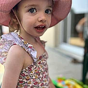 Victoire a rejoint le concours — aidez-le/la à gagner de superbes lots ! child, toddler, pink_hat, floral_dress, outdoor, portrait, curious_expression, summer, sunhat, face, eye_contact, closeup, soft_background, person, smile, cute, young_child, daylight, fashion, playful