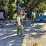toddler, child, hoodie, socks, toy, outdoor, patio, chairs, umbrella, sunlight, shadow, trees, greenery, paved_floor, playful, curious, daylight, casual_clothing, baby, person