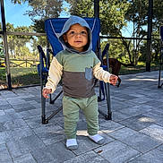 Arlo joined the competition — help win amazing prizes! toddler, child, hoodie, outdoor, patio, paved_floor, folding_chair, dog, trees, sunlight, greenery, casual_clothing, socks, person, daylight, nature, backyard, cute, standing, smiling