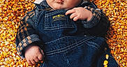 Briceson is registered to the contest to win money with this photo: baby, beanie, child, closeup, clothing, corn, corn_kernels, denim, eyes, face, golden, hand, infant, jacket, lying_down, outdoor, overalls, photography, portrait, texture