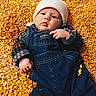 baby, beanie, child, closeup, clothing, corn, corn_kernels, denim, eyes, face, golden, hand, infant, jacket, lying_down, outdoor, overalls, photography, portrait, texture