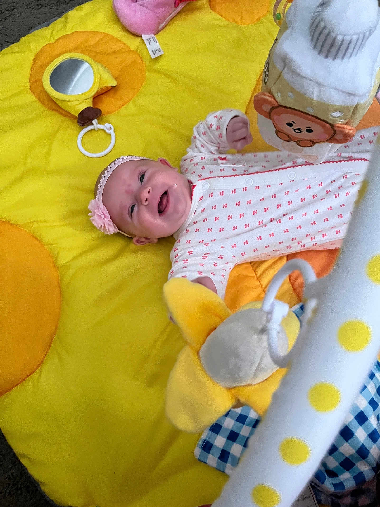 Charlotte is registered to the contest to win money with this photo: baby, infant, playmat, yellow, toy, plush, mirror, headband, smiling, onesie, hand, happy, child, floor, cute, indoor, pattern, soft, reaching, lying