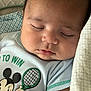 baby, sleeping, infant, face, clothing, mickey_mouse, cartoon, tennis_racket, blue_shirt, blanket, closeup, child, cute, peaceful, resting, soft_texture, indoors, portrait, skin, eyelashes