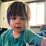 Deca is registered to the contest to win money with this photo: toddler, child, portrait, indoor, casual_clothing, teal_shirt, face, hair, window, blinds, soft_light, curious_expression, young_child, sitting, home, blurry_background, person, close_up, young_kid, candid