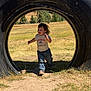 child, toddler, running, tire, outdoor, grass, field, sky, trees, blue_sky, jeans, tshirt, smiling, sunlight, nature, playground, happy, daytime, casual_clothing, fun