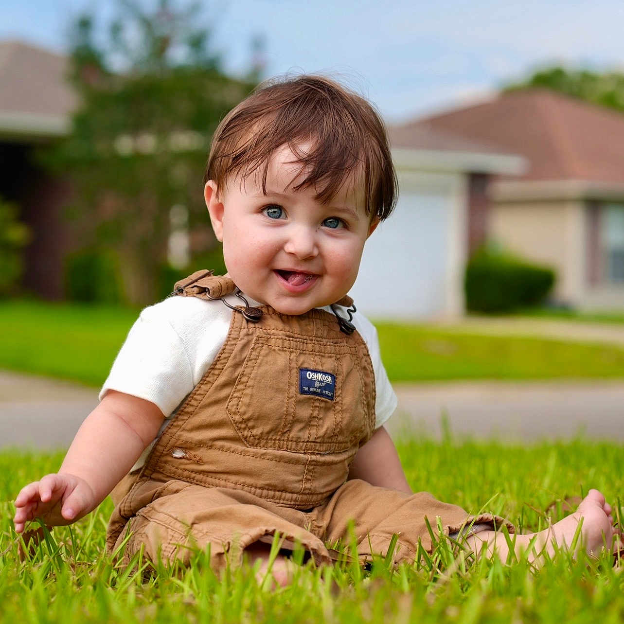 Jaxson joined the competition — help win amazing prizes! toddler, child, grass, outdoor, smiling, barefoot, overalls, short_sleeves, blue_eyes, brown_hair, house, suburban, daylight, greenery, happy, sitting, portrait, nature, casual_clothing, playful