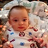 baby, casual_clothing, child, closeup, comfortable, cushion, cute, expressionless, face, heart_overlay, indoors, infant, onesie, patterned_cushion, person, portrait, sitting, soft_lighting, spiderman, young_child