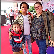 Juan a rejoint le concours — aidez-le/la à gagner de superbes lots ! adult, background, banner, casual_clothing, child, event, footwear, glasses, group, happy, hat, jacket, outdoor, people, posing, red_carpet, smiling, standing, tent, tree