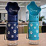 blue, branding, cat_logo, desk, hydration, indoor, lid, matching_pair, modern, office, paw_print, pet_accessory, pet_bottle, plastic, product_photography, strap, table, transparent, turquoise, water_bottle