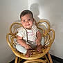 baby, child, smile, wicker_chair, furniture, indoor, happy, cute, person, clothing, toddler, foot, hand, seat, wall, shadow, head, face, pants, shirt