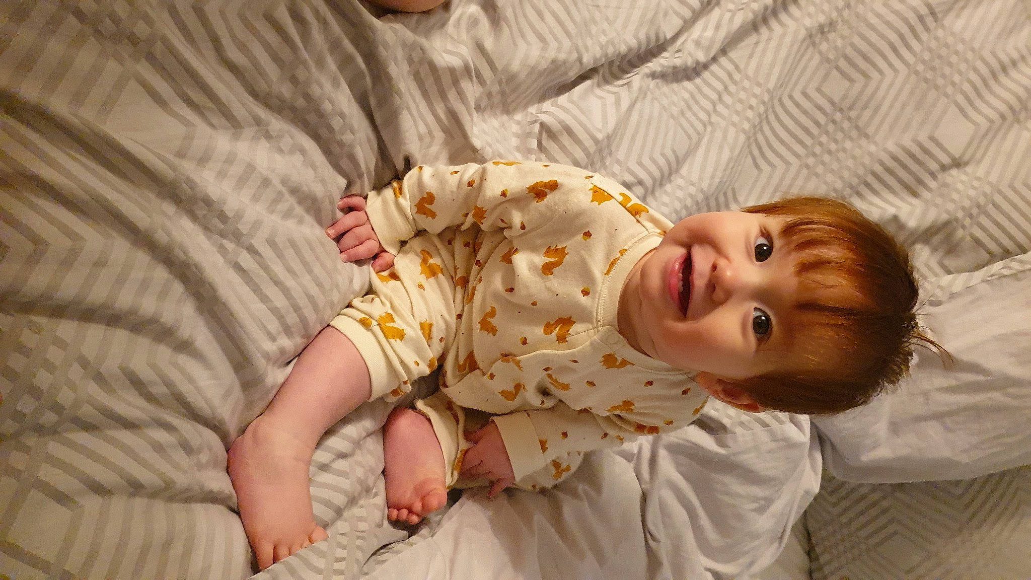 Callum is registered to the contest to win money with this photo: baby, baby_toddler_clothing, child, comfort, face, flooring, fun, happy, head, human_body, joy, linens, nose, orange, pattern, person, sitting, skin, sleeve, smile