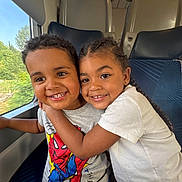 Lewis a rejoint le concours — aidez-le/la à gagner de superbes lots ! child, children, smiling, hug, train, window, seat, clothing, tshirt, braids, short_hair, happy, portrait, travel, indoor, boy, girl, friendship, cute, people