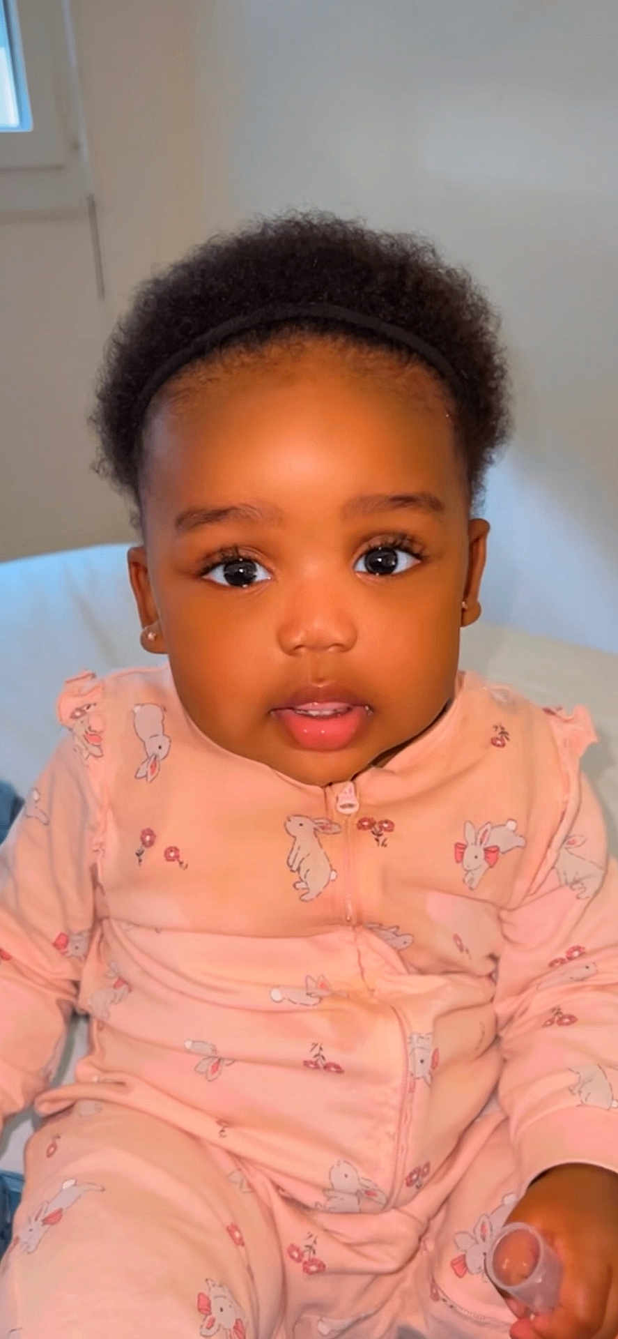 Keyliah Elora participe au concours pour gagner de l'argent avec cette photo : toddler, baby, child, face, eyes, pink_clothing, onesie, bunny_pattern, indoor, portrait, curly_hair, headband, sitting, hand, expression, cute, young, person, skin, earrings