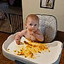 baby, child, highchair, tray, food, macaroni, peas, mess, eating, socks, bare_torso, face, big_eyes, wooden_floor, framed_photos, wall, living_room, curtain, baby_gate, stool
