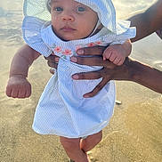 Imani is registered to the contest to win money with this photo: baby, child, infant, beach, sand, sunhat, dress, hands, feet, outdoor, sunlight, portrait, person, summer, cute, young_child, skin, blue_eyes, stripes, nature