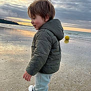 Liam participe au concours pour gagner de l'argent avec cette photo : child, boy, jacket, pants, sneakers, beach, sand, sea, sunset, clouds, yellow_ball, water, shore, walking, outdoor, nature, sky, reflection, happy, play