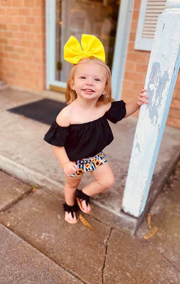 Brenley is registered to the contest to win money with this photo: baby, child, clothing, event, eye, face, fashion_accessory, fun, grass, hairstyle, happy, headband, human_leg, joy, leisure, person, pink, recreation, sandal, sitting