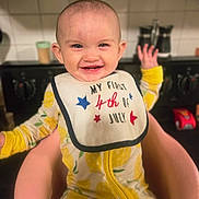 Luna joined the competition — help win amazing prizes! baby, child, smile, bib, yellow, onesie, lemon_pattern, chair, kitchen, stove, happy, portrait, infant, person, indoor, cute, celebration, holiday, first_birthday, sitting