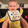 baby, child, smile, bib, yellow, onesie, lemon_pattern, chair, kitchen, stove, happy, portrait, infant, person, indoor, cute, celebration, holiday, first_birthday, sitting