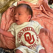Oaklee is registered to the contest to win money with this photo: baby, newborn, infant, blanket, heart_pattern, clothing, onesie, person, face, head, skin, hair, lying_down, soft_texture, cozy, pink, white, logo, indoor, cute