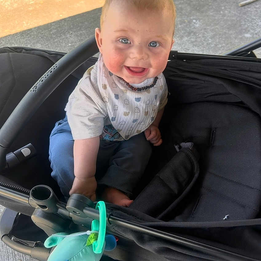 Richie is registered to the contest to win money with this photo: baby, car, clothing, coat, face, glove, grass, happy, head, jacket, pants, person, photography, plant, portrait, smile, stroller, t_shirt, transportation, vehicle