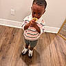Saint is registered to the contest to win money with this photo: child, boy, toddler, portrait, standing, eating, snack, food, yellow_food, striped_shirt, polo_shirt, shorts, sneakers, wooden_floor, indoor, home, mirror, wall, outlet, focused