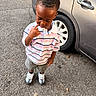 child, toddler, boy, portrait, standing, outdoor, parking_lot, car, vehicle, asphalt, striped_shirt, polo_shirt, shorts, sneakers, fashion, looking_down, thoughtful, daylight, face, street