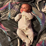 Elias is registered to the contest to win money with this photo: baby, infant, onesie, blanket, pattern, laying_down, curious, face, person, child, indoor, fabric, colorful, expression, sleepwear, newborn, cute, soft, comfort, portrait