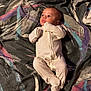 baby, infant, onesie, blanket, pattern, laying_down, curious, face, person, child, indoor, fabric, colorful, expression, sleepwear, newborn, cute, soft, comfort, portrait