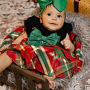 Angelina joined the competition — help win amazing prizes! baby, child, infant, green_bow, plaid_dress, wooden_bed, blanket, gift_box, earrings, holiday, festive, carpet, smiling, cute, indoors, portrait, wrapped_presents, floor_rug, cozy, happy